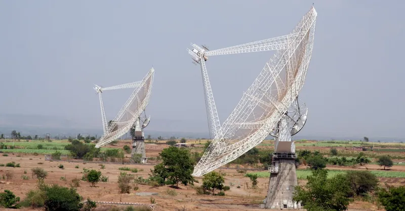 Two large satellite dishes in a rural field near Pune, India, capturing signals.