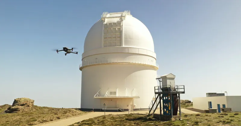 A drone flies by a large observatory dome under a clear blue sky. Technology meets astronomy.