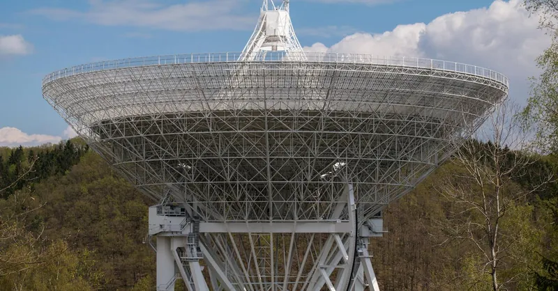 A large radio telescope set against a backdrop of trees and clouds, capturing celestial signals.