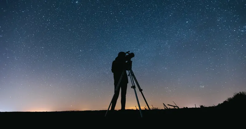 Silhouette of a person using a telescope under a starry night sky, perfect for astronomy themes.
