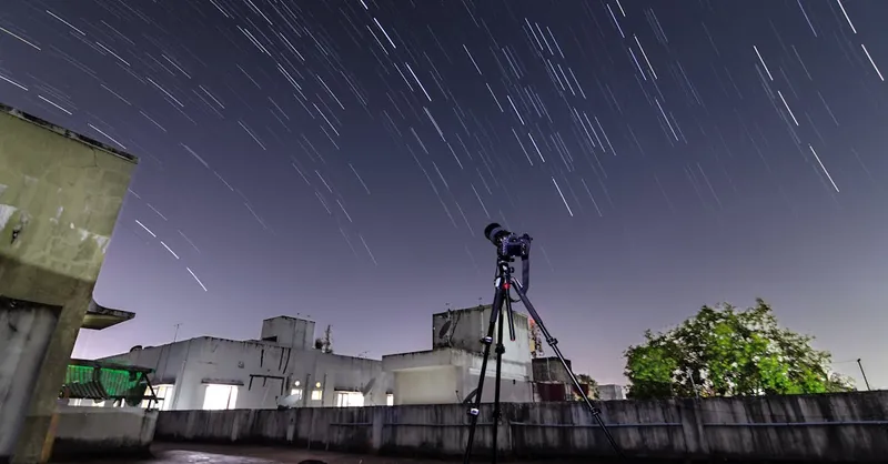 A telescope on a rooftop captures star trails in the night sky.