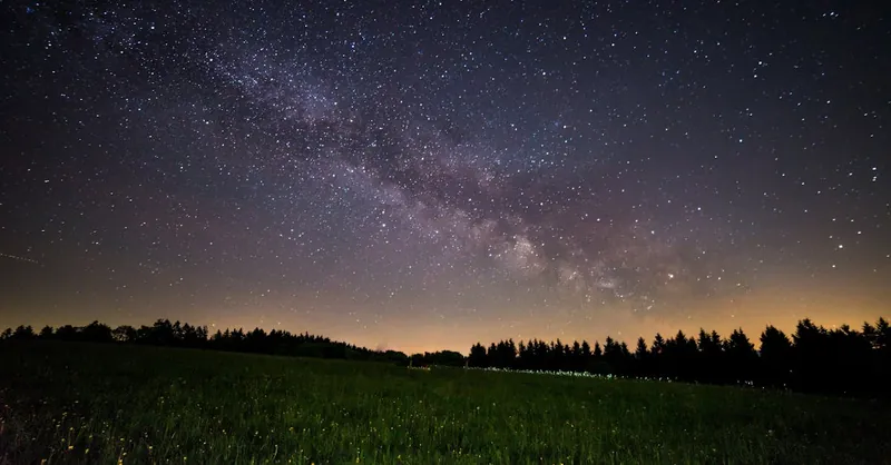 A breathtaking view of a starry night sky over a quiet field, showcasing the Milky Way.