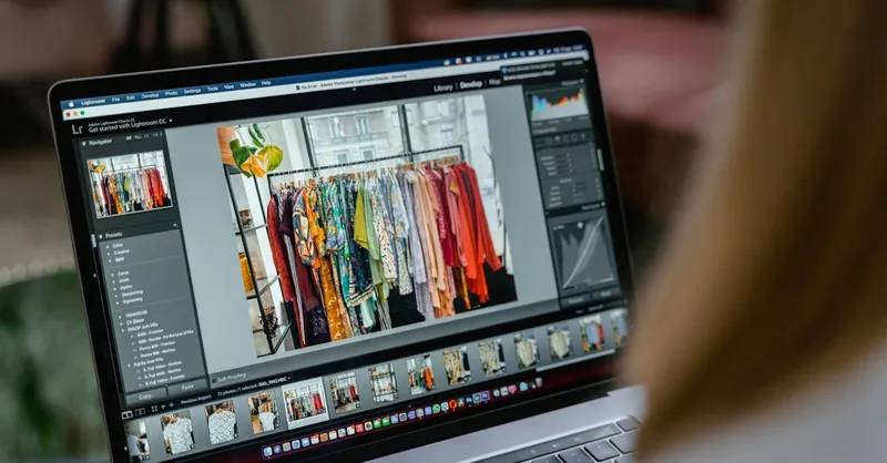 Close-up of a laptop displaying photo editing software with clothes rack in view.