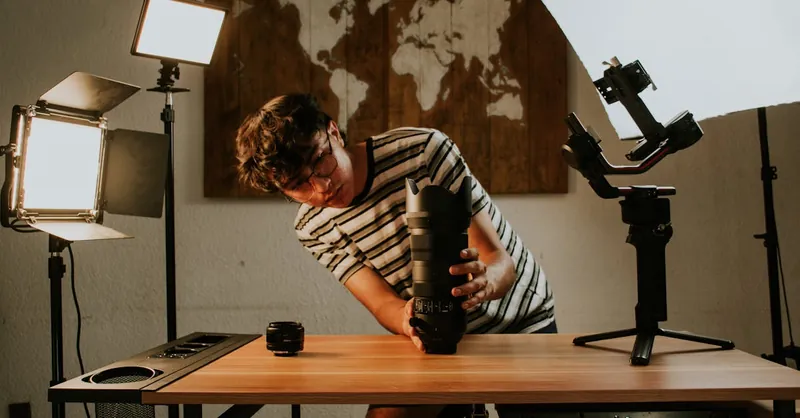 A photographer preparing camera gear in a studio with professional lighting setup and lens.