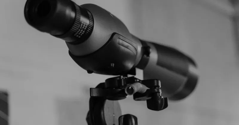 Detailed monochrome image of a modern telescope lens mounted on a tripod.
