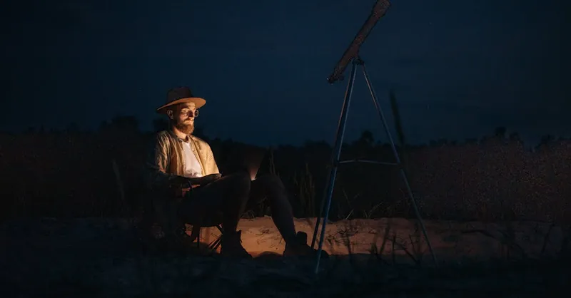 A man with a laptop explores the night sky with a telescope, capturing the essence of digital nomad life.