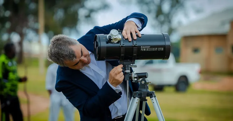 Adult man using a telescope outdoors during the day, engaged in astronomy.