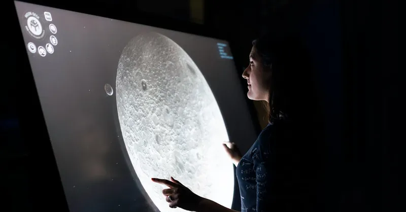 A woman interacts with a touchscreen showing the moon