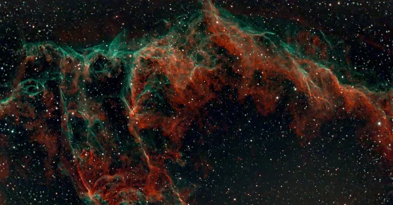 Captivating image of the Veil Nebula showing vibrant red and green hues against the starry cosmos.