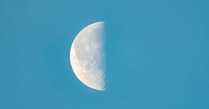 Detailed photo of the half moon in daylight sky, showcasing lunar surface features.