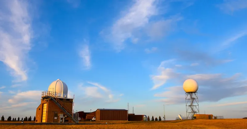 Weather radar station set in a field with a clear blue sky and scattered clouds, showcasing meteorological technology.