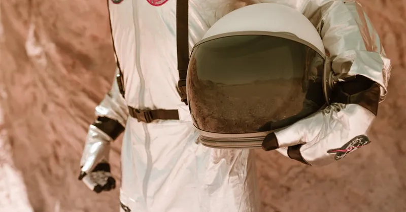 An astronaut in a reflective spacesuit holding a helmet, standing in a desert landscape resembling Mars.