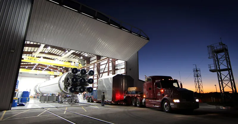 A large rocket being moved from a hangar at twilight, showcasing advanced engineering and space technology.