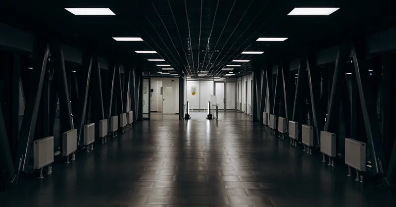 Spacious modern long corridor with clean floor with tile and luminous lamps in darkness