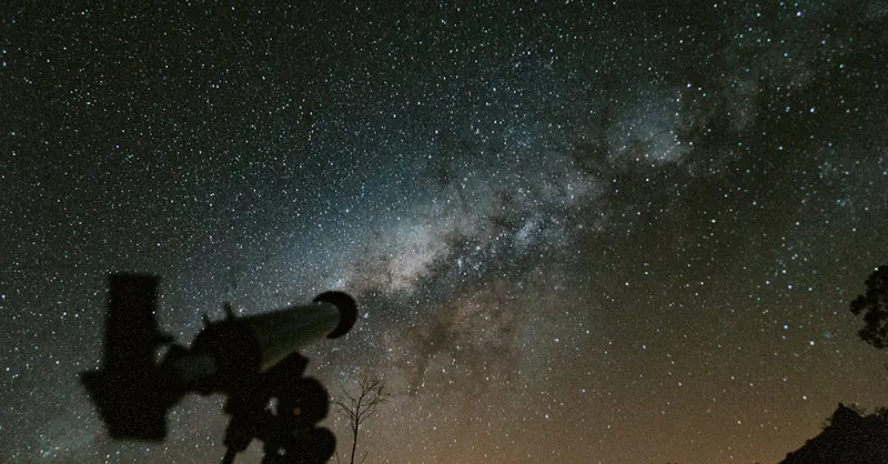Silhouette of a telescope with a stunning Milky Way background in the night sky.