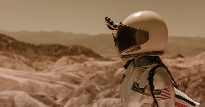 An astronaut in a space suit explores a desolate rocky landscape under a bright sky.