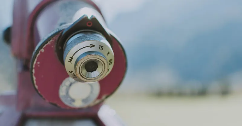 Detailed close-up of an outdoor telescope lens with a blurred natural background.