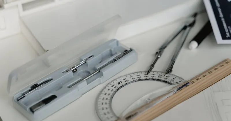 Close-up of architectural drafting tools including compasses, ruler, and paper on a workspace table.