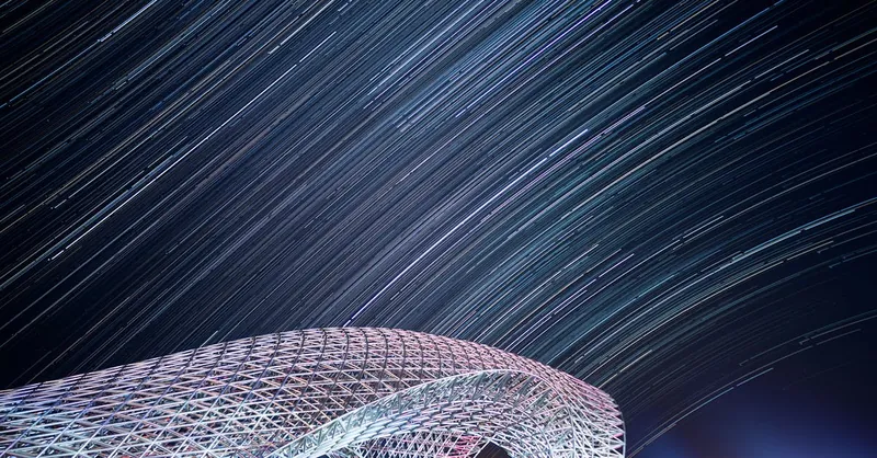 A stunning view of modern architecture beneath a star-filled night sky with visible star trails.