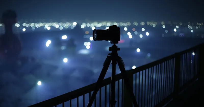 Silhouette of a camera on a tripod capturing city lights at night.