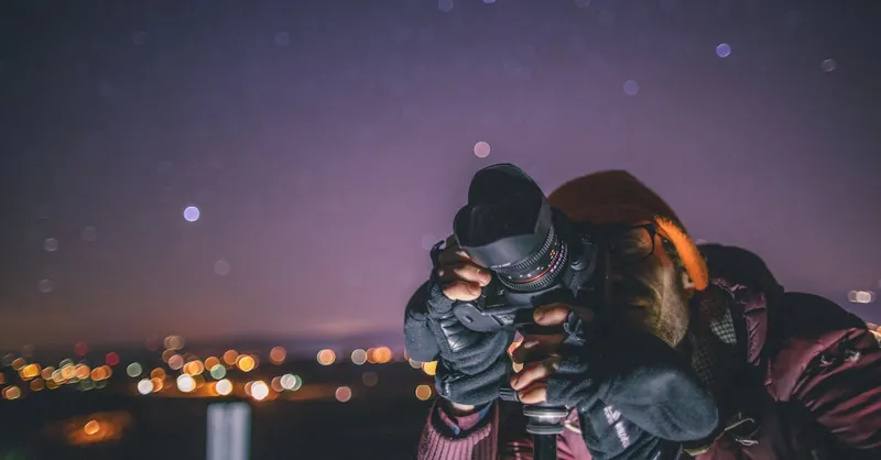 Photographer capturing night sky, surrounded by stars and city lights.