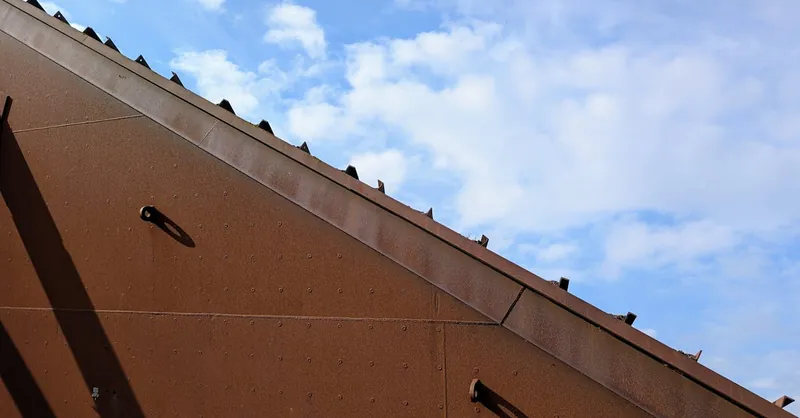 Close-up of a rusty metal roof with a blue sky backdrop, showcasing industrial texture.